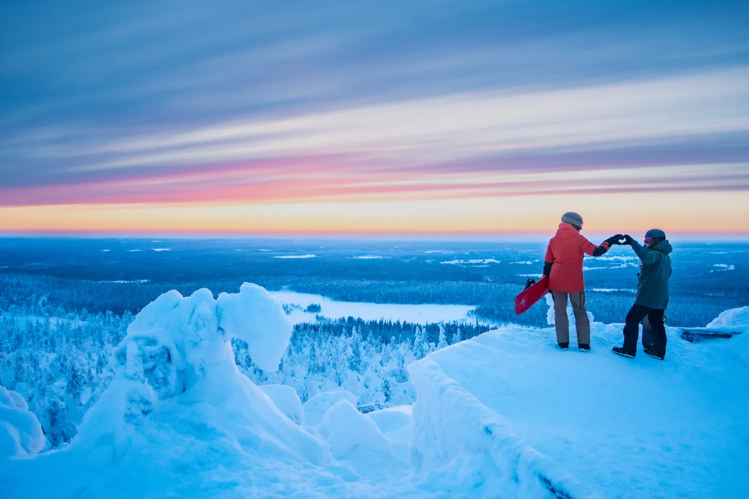 Tunturin huipulla kaksi ihmistä tekee käsillään sydäntä auringonlaskussa