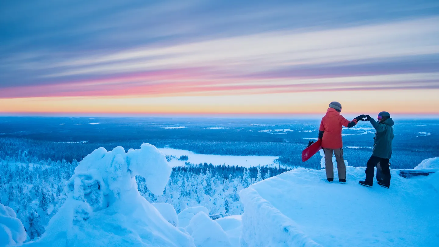 Tunturin huipulla kaksi ihmistä tekee käsillään sydäntä auringonlaskussa